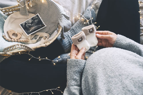Pregnant woman holding tiny socks with holiday lights and ultrasound in picture